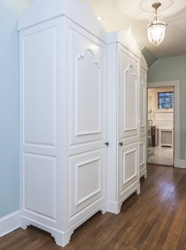A custom paneled built-in wardrobe wall in white, opening toward a soft blue bedroom.