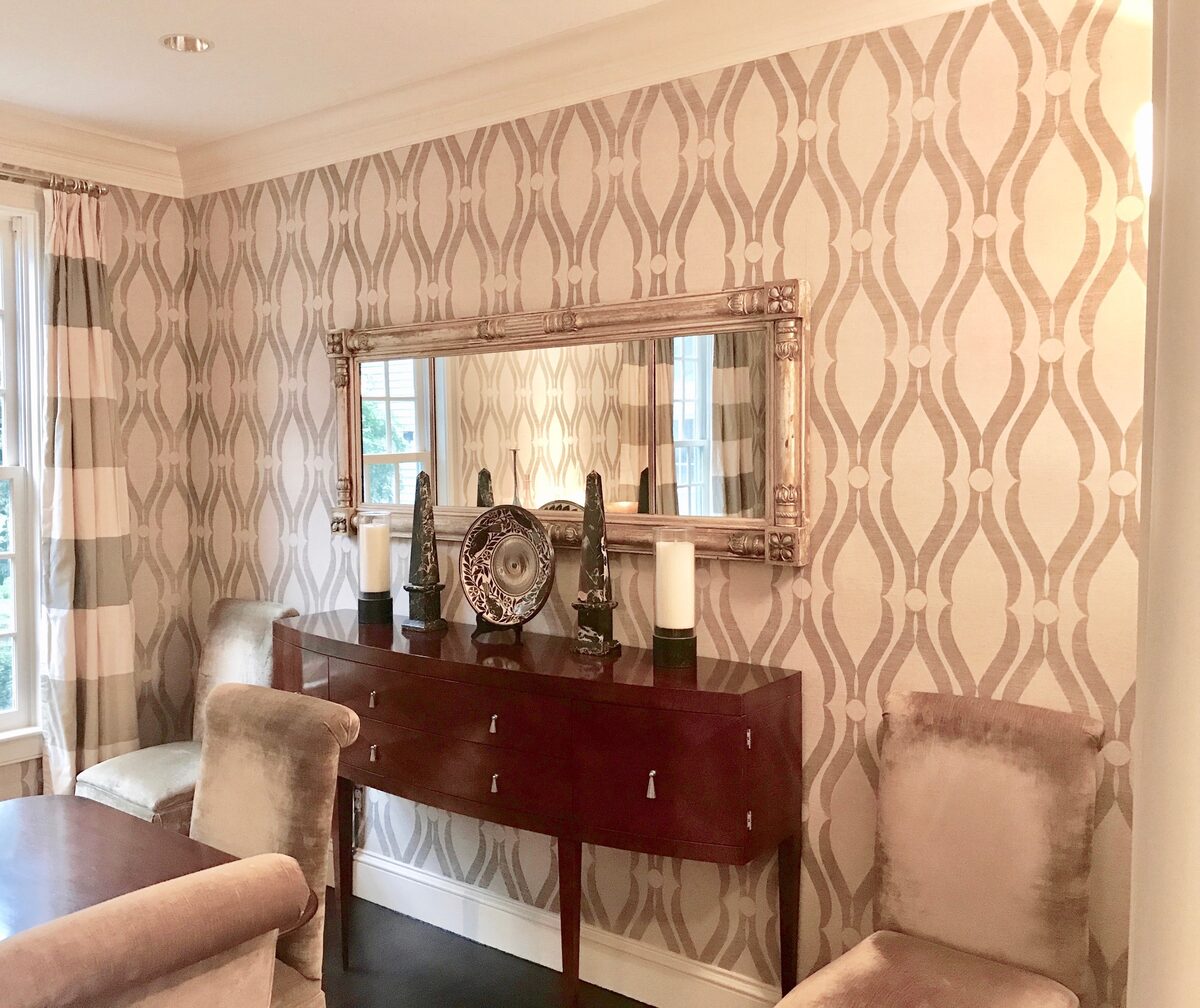 A dining vignette anchored by a patterned wallpaper, an antique mirror, and a collected sideboard.