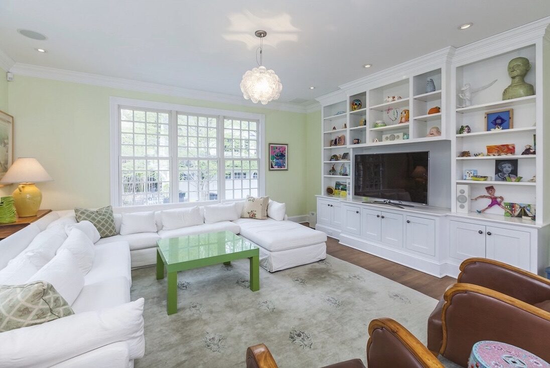 A bright family room with a white sectional and a wall of custom built-in shelving around the TV.