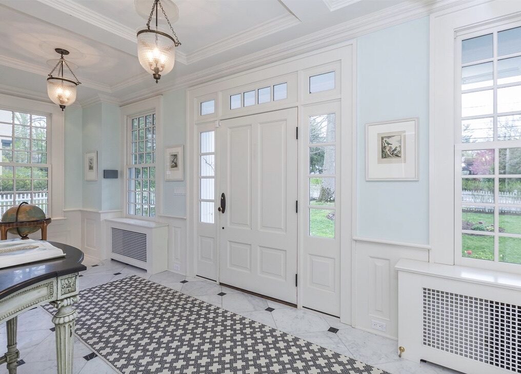 A sky-blue foyer with marble floors, a paneled front door, and a graphic patterned runner.