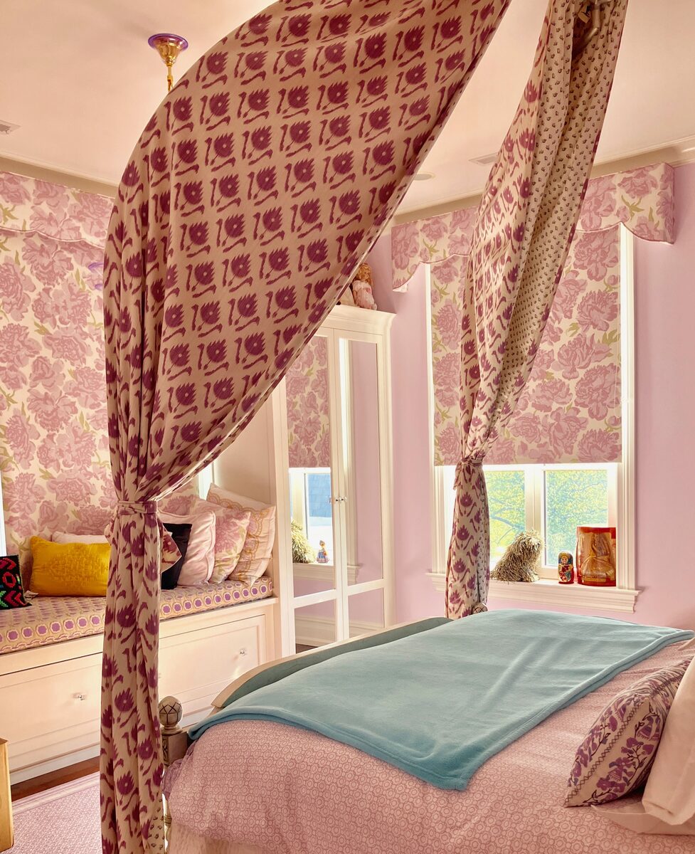 A romantic girls' room with a rose-print canopy bed, a window seat, and soft pink walls.