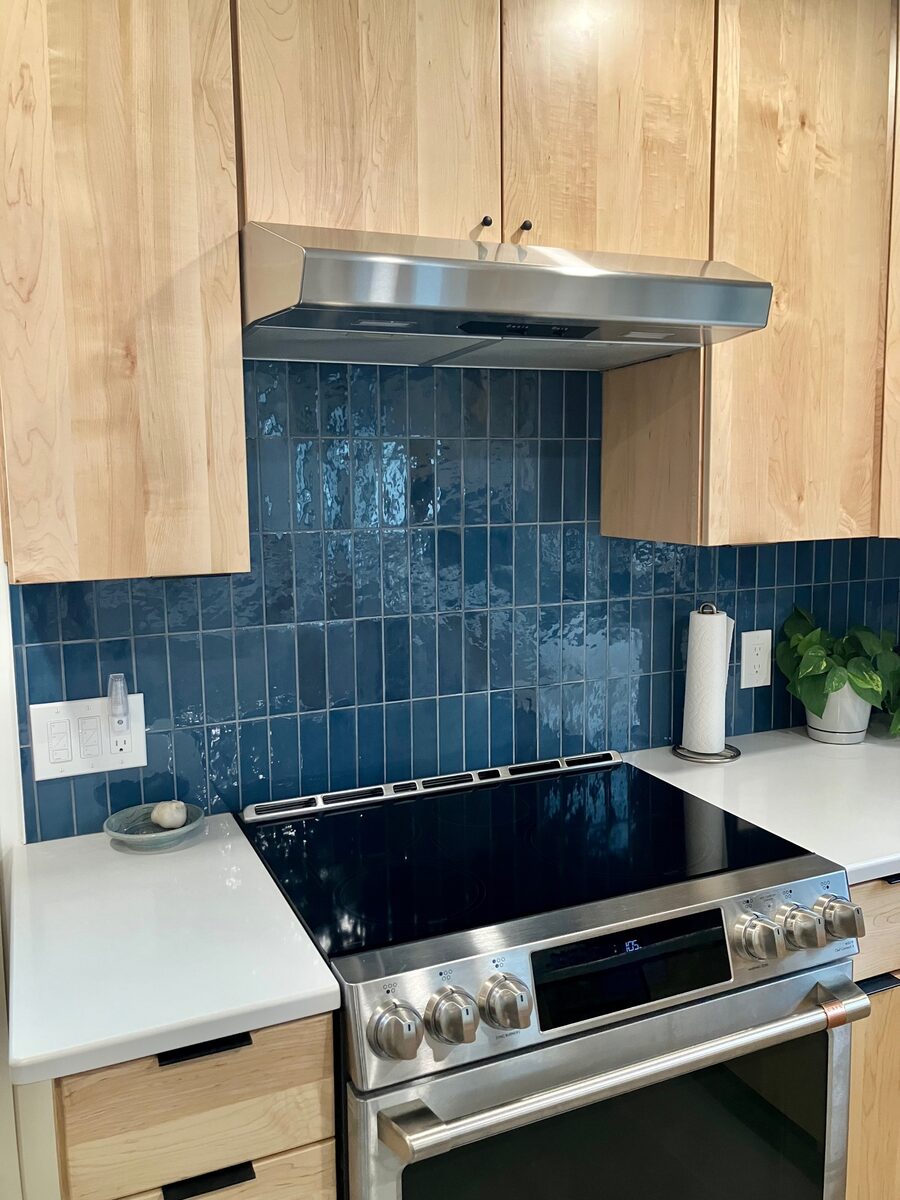 A warm kitchen with a blue patterned tile backsplash and natural maple cabinetry.