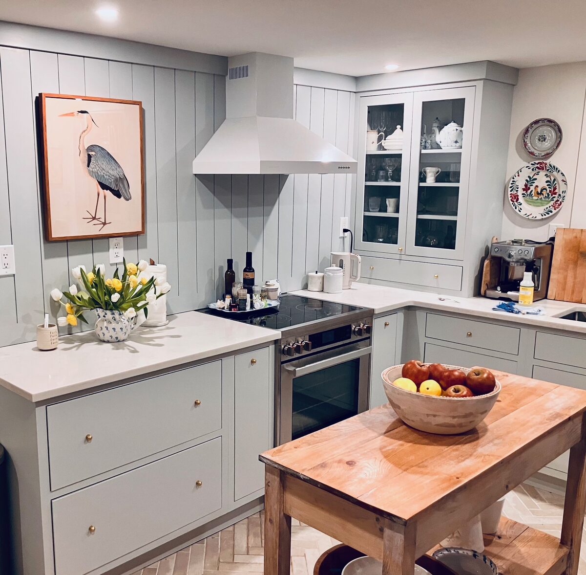 A blue-gray kitchen with a built-in glass cabinet, shiplap walls, and a great-blue-heron print.