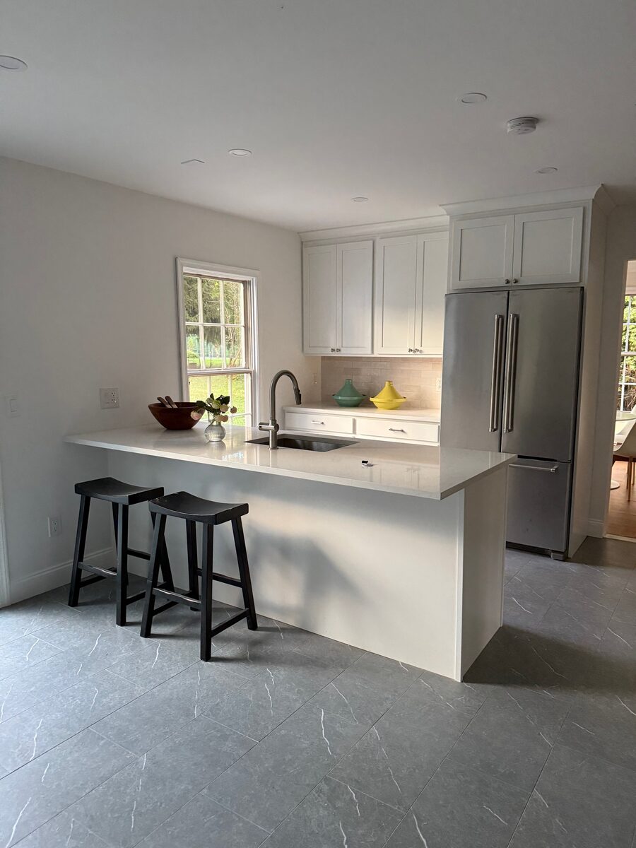 A minimalist's white kitchen with quartz countertops, black saddle stools, and soft grey floors.