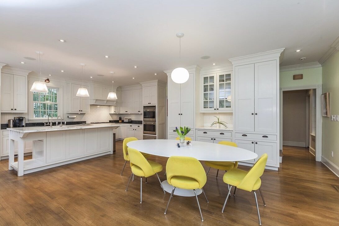 An open white kitchen paired with an oval table and sunny yellow Saarinen-style chairs.