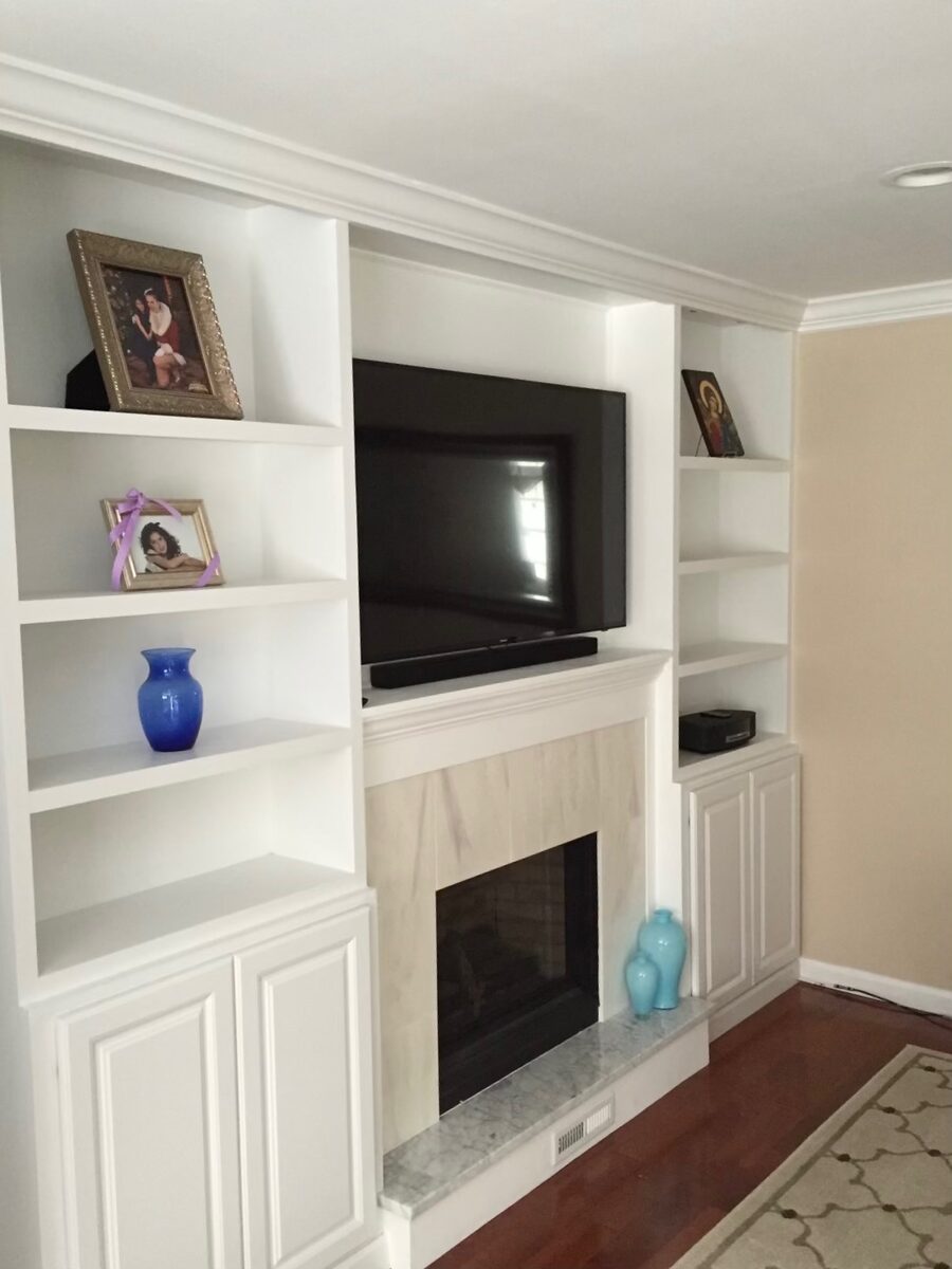 Custom built-in shelving and cabinetry flanking a marble fireplace and mounted television.