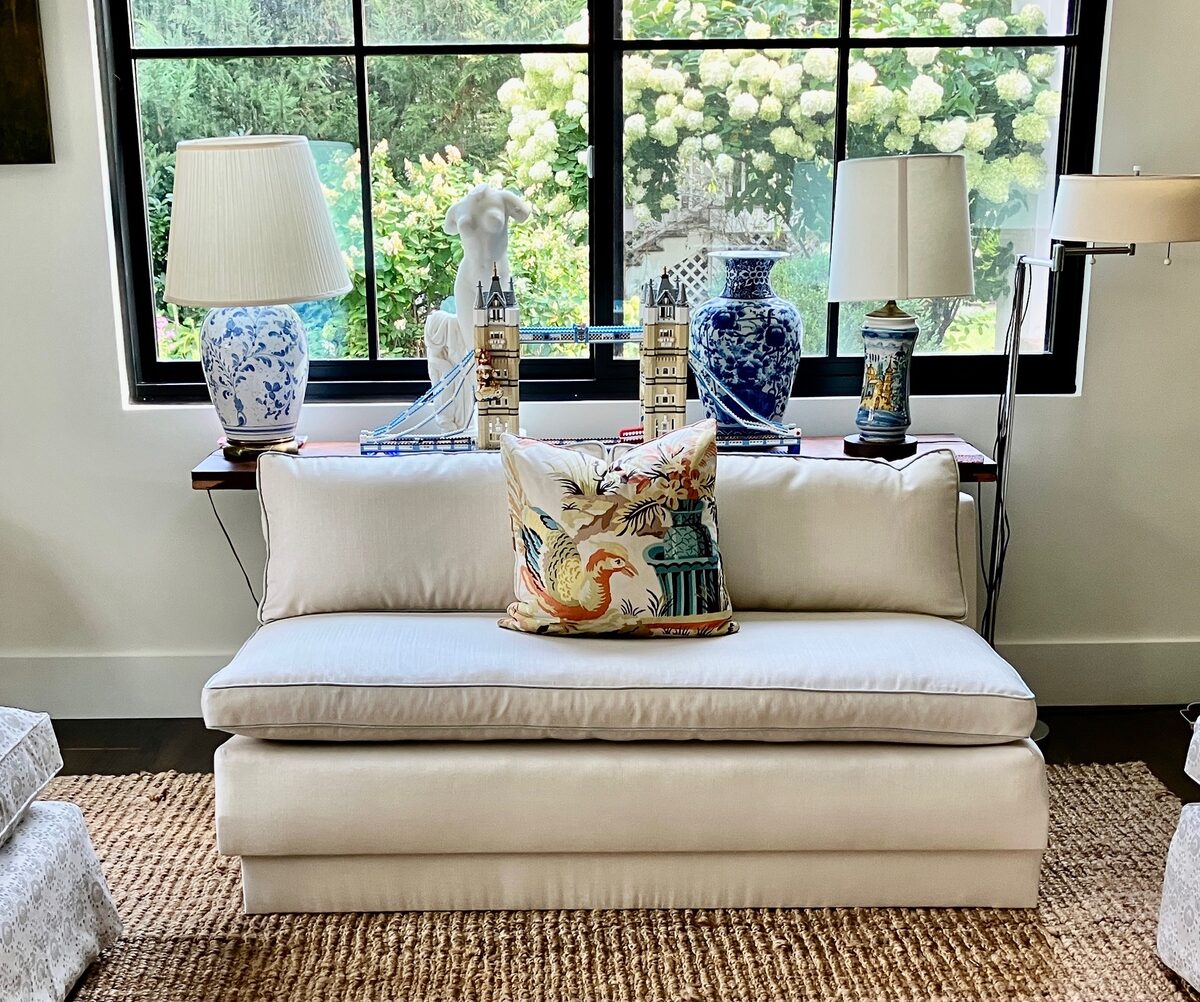 A crisp white settee beneath a black-framed window, styled with blue-and-white lamps and a vivid pillow.