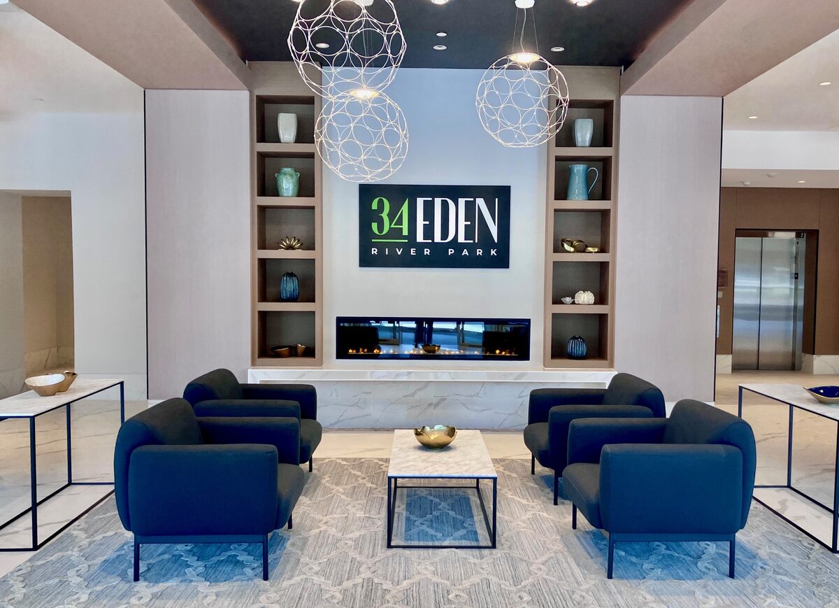 Blue lounge chairs gathered around a marble fireplace beneath statement lighting in a building lobby.