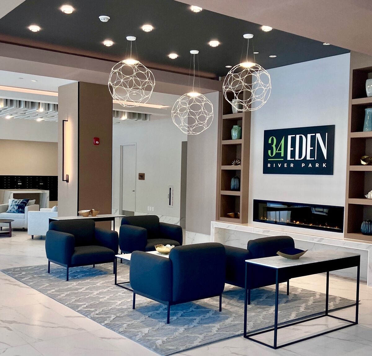 A contemporary residential lobby with sculptural orb pendants, a linear fireplace, and deep blue seating.