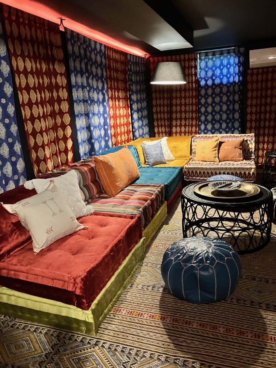 A jewel-toned media lounge with low floor cushions, layered textiles, and a Moroccan pouf.