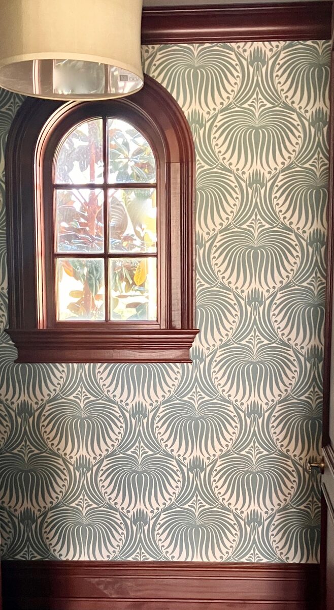 A jewel-box powder room wrapped in graphic green wallpaper with a richly stained arched window.