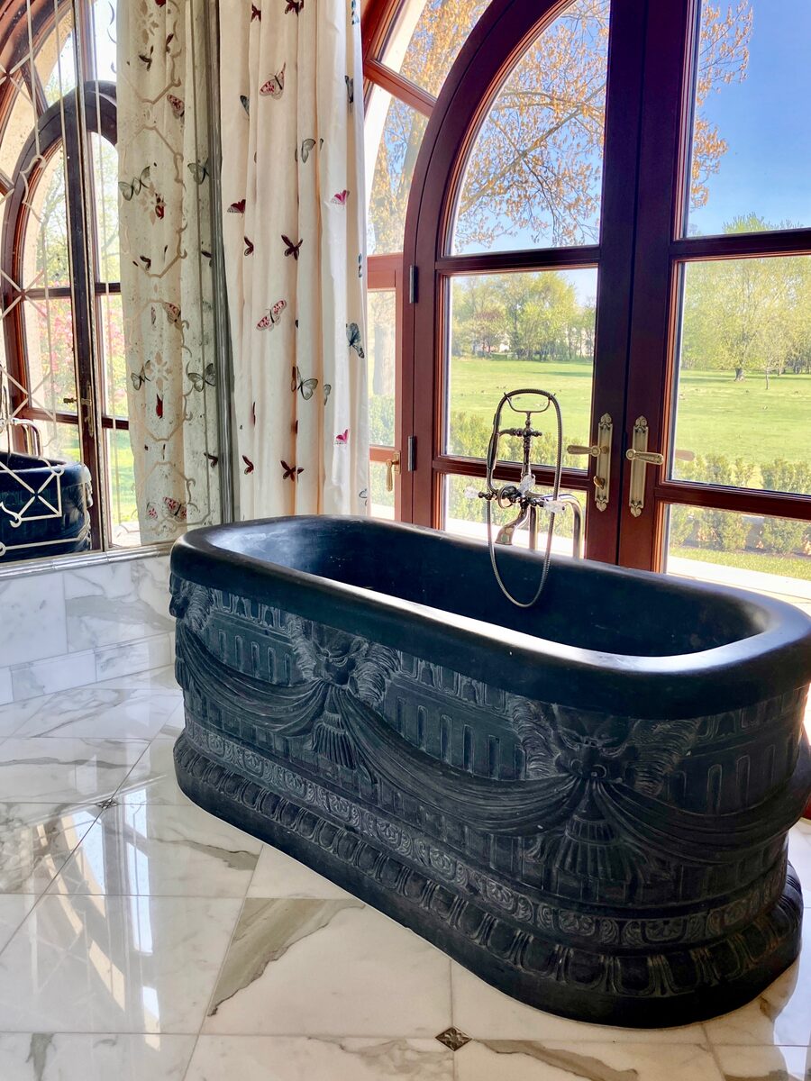 Another view of the carved soaking tub, framed by butterfly-embroidered drapery and bright marble.