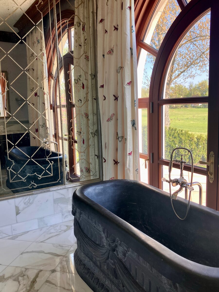 A sculptural black soaking tub set before arched windows overlooking the lawn, grounded in marble.