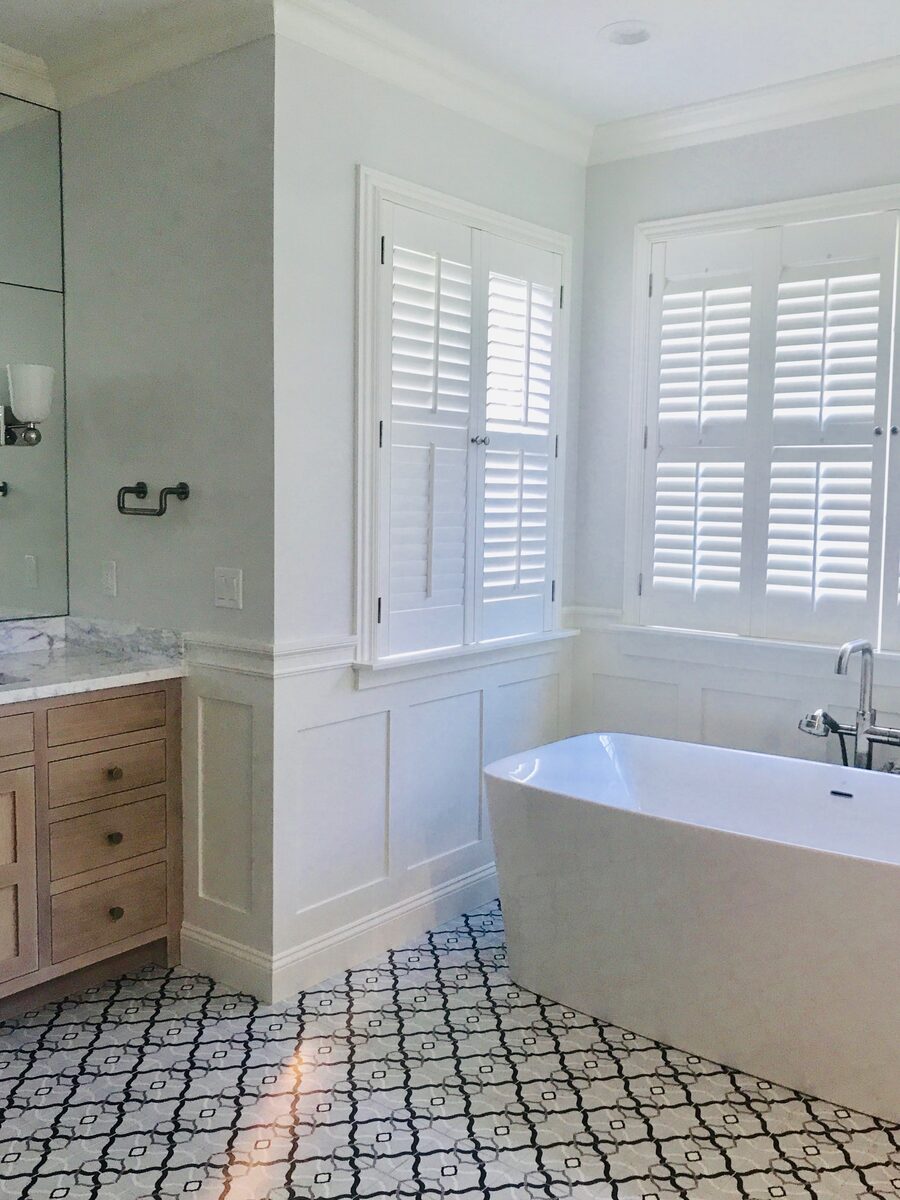 A serene primary bath with a freestanding tub, plantation shutters, and a patterned mosaic floor.