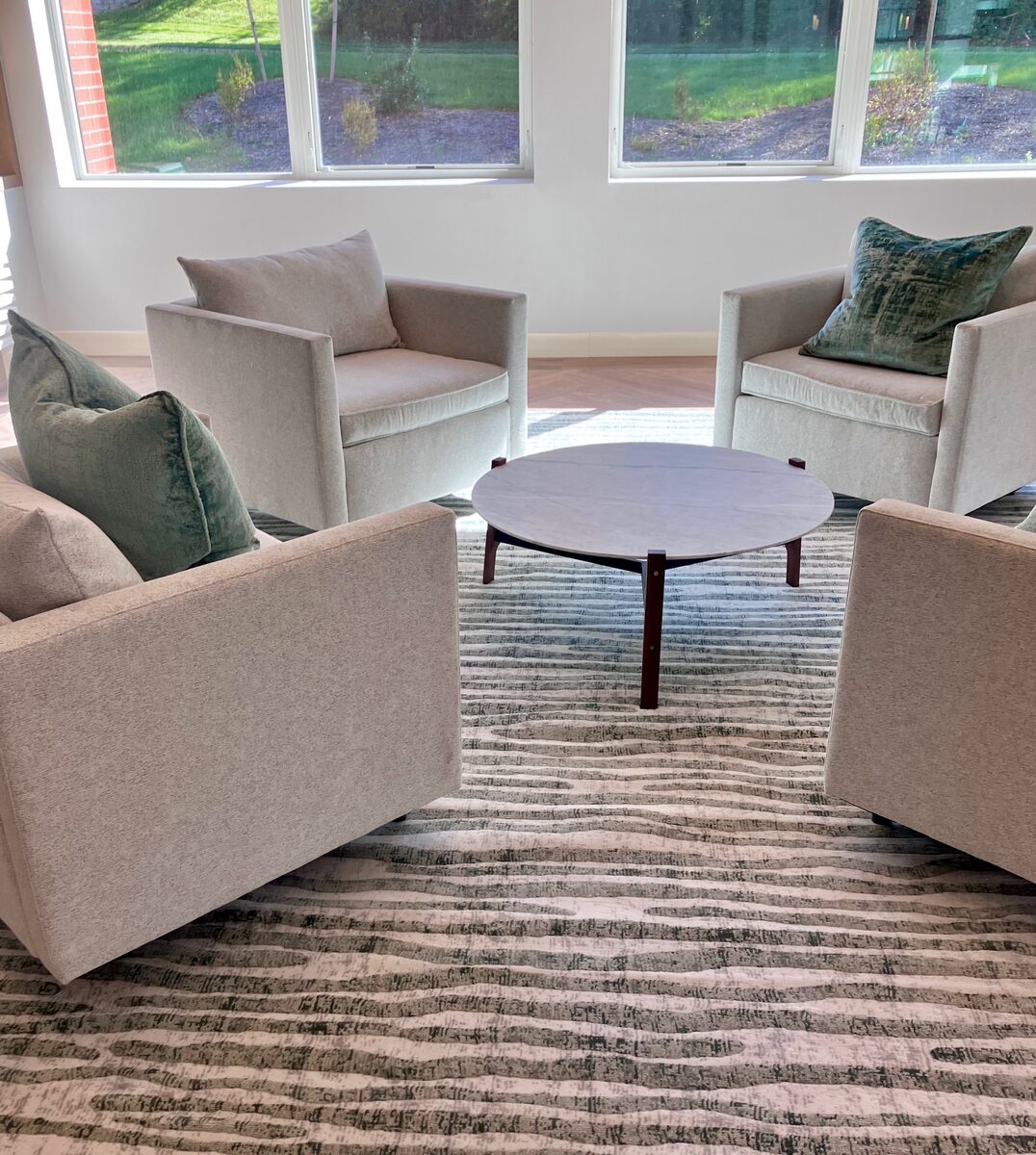 A resident lounge in soft neutrals with built-in shelving, blue accent pillows, and an oak coffee table.