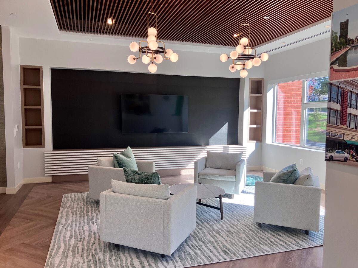 A media lounge with a slatted wood ceiling, globe chandeliers, and a relaxed cluster of armchairs.
