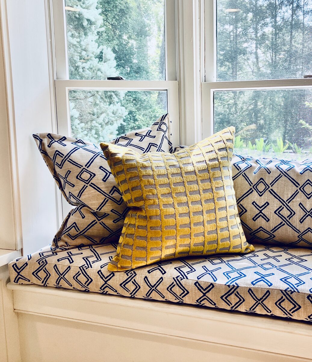 A close study of mixed pillows in blue and gold against a sunlit window seat.